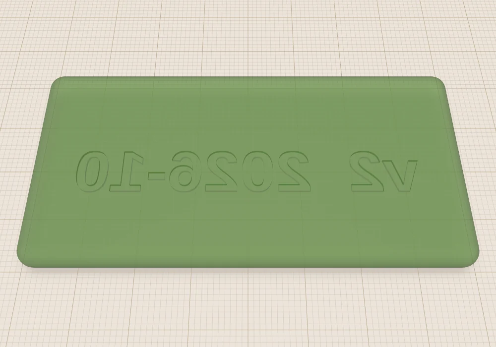 A see-through green plate seen from above, with the text v2 2026-10 engraved in its bottom face, reading backwards.
