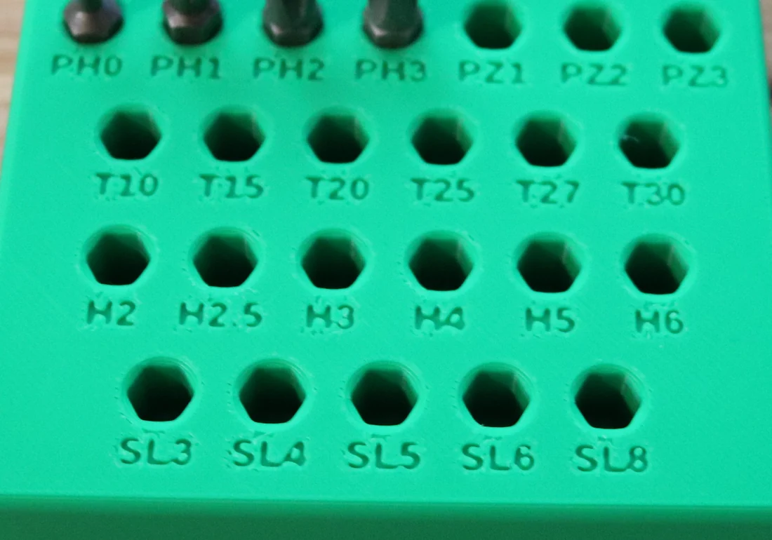 A photo of the printed green bit holder: rows of hex pockets, each with a small engraved label such as PH2, T20, H2.5 and SL6.
